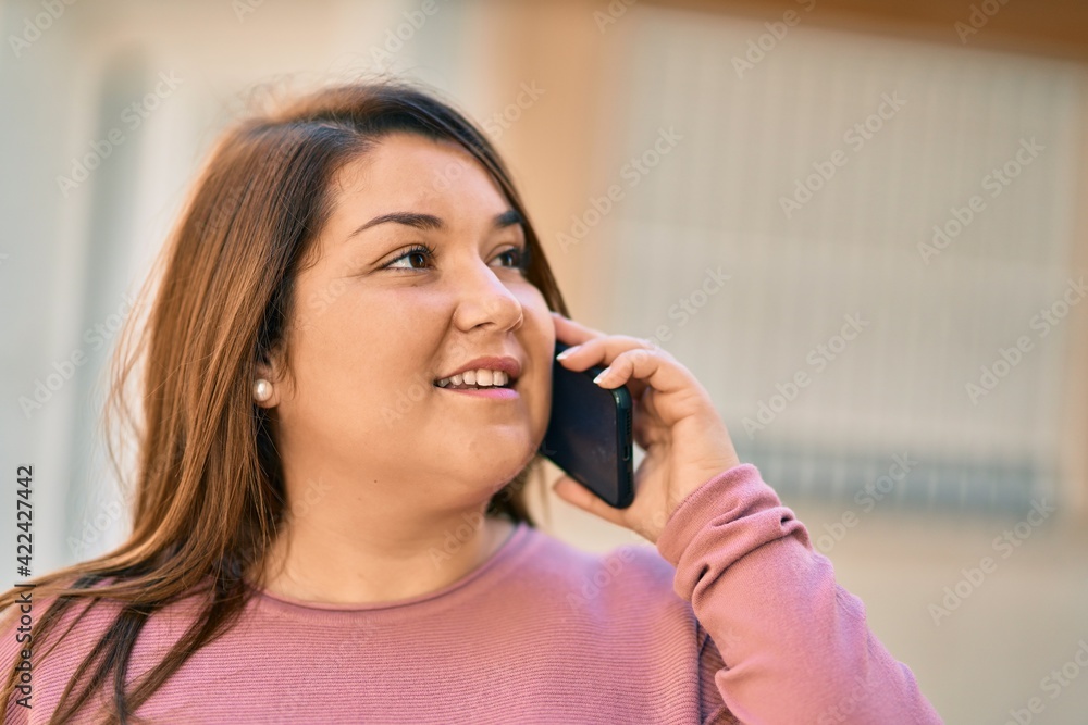 Young plus size woman smiling happy talking on the smartphone at the city. Young plus size woman smiling happy talking on the smartphone at the city.