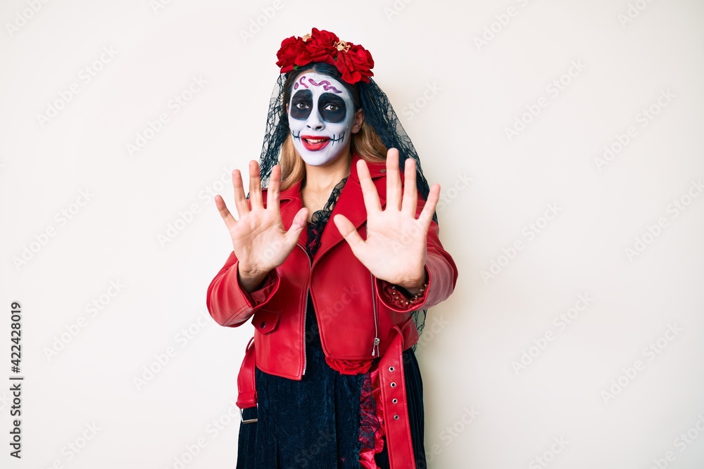 Woman wearing day of the dead costume over white afraid and terrified with fear expression stop gesture with hands, shouting in shock. panic concept. Woman wearing day of the dead costume over white afraid and terrified with fear expression stop gesture with hands, shouting in shock. panic concept.