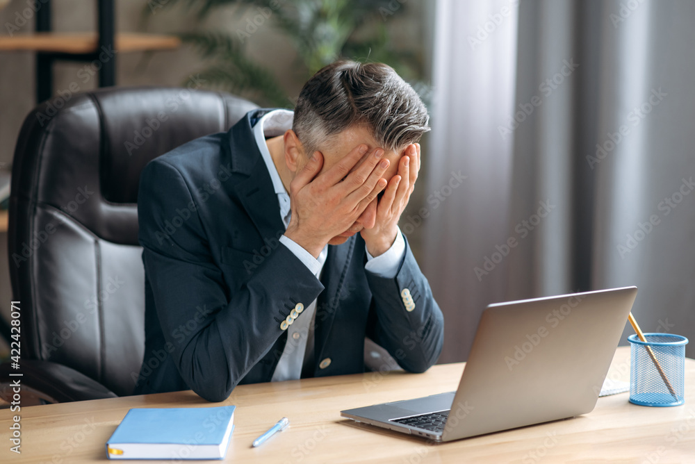 Exhausted caucasian gray haired business leader, manager, ceo in formal suit is sitting in the office, he has a headache, tired or stressed, covers his face with his hands, need rest or break Exhausted caucasian gray haired business leader, manager, ceo in formal suit is sitting in the office, he has a headache, tired or stressed, covers his face with his hands, need rest or break
