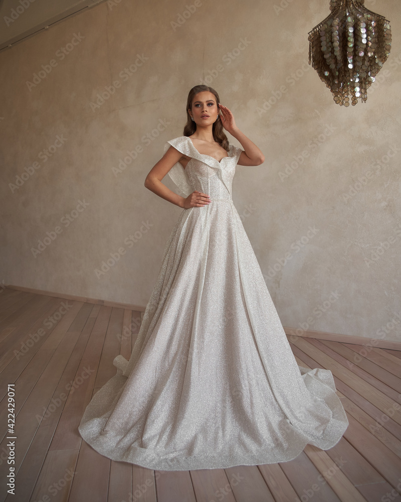 Full length bride portrait. Elegant woman in white wedding dress spinning in beige interior. Dynamic shot. Elegant female model standing and posing in ball gown Full length bride portrait. Elegant woman in white wedding dress spinning in beige interior. Dynamic shot. Elegant female model standing and posing in ball gown