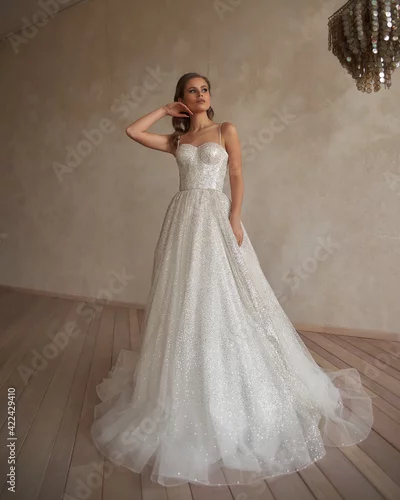 Obraz Full length portrait of young beautiful woman wearing white wedding dress. Elegant bride standing and posing against beige wall