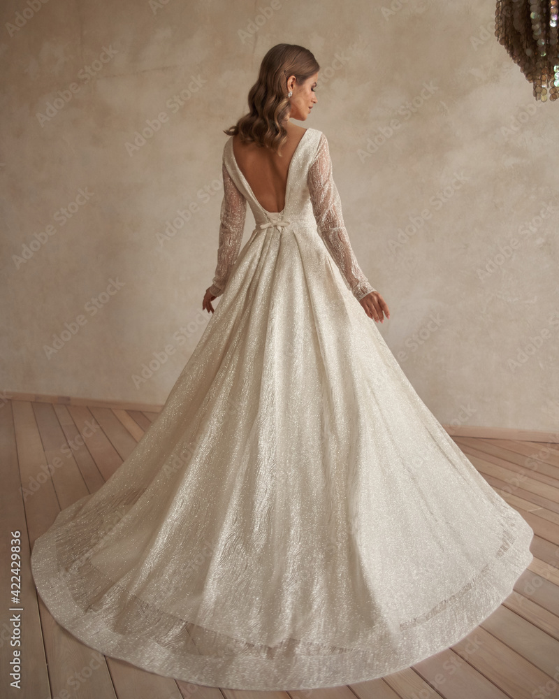 Full length portrait of young beautiful woman wearing white wedding dress. Elegant bride standing and posing against beige wall Full length portrait of young beautiful woman wearing white wedding dress. Elegant bride standing and posing against beige wall