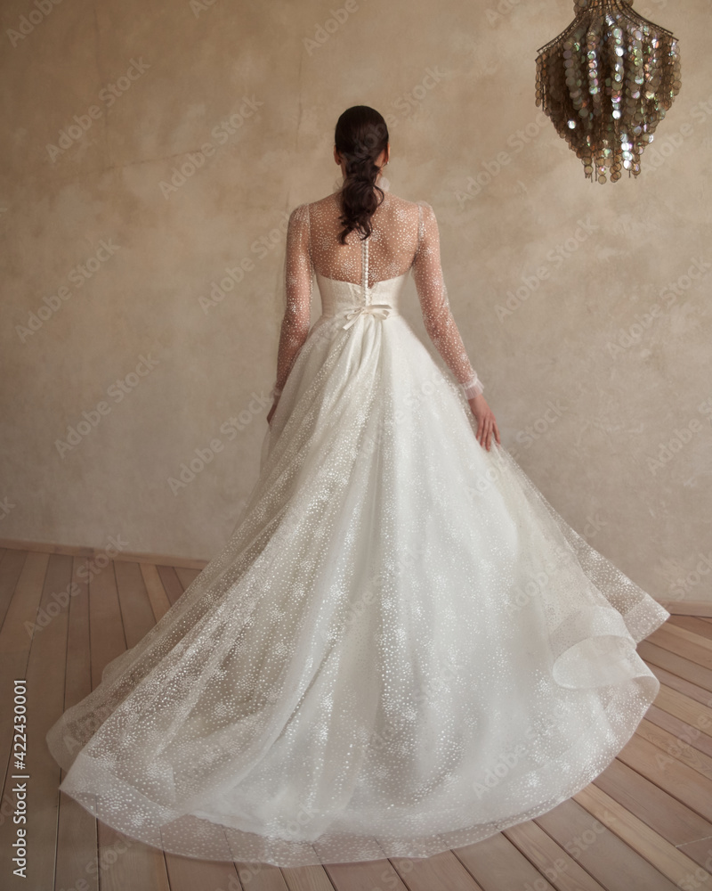 Full length portrait of young beautiful woman wearing white wedding dress. Elegant bride standing and posing against beige wall Full length portrait of young beautiful woman wearing white wedding dress. Elegant bride standing and posing against beige wall