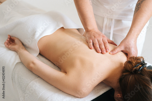 Top view of male masseur doing back massage to young unrecognizable young woman in spa salon. Professional physiotherapist with strong hands making movements with hand along the spine toward head.