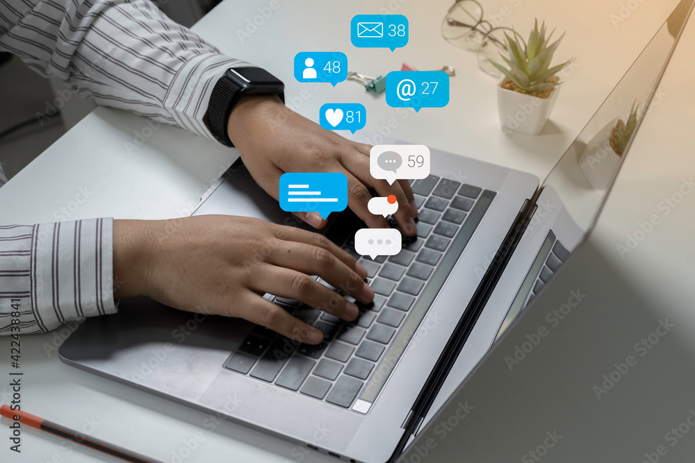 Person using a social media marketing concept on laptop with notification icons of like, chat, message and comment above laptop screen. Person using a social media marketing concept on laptop with notification icons of like, chat, message and comment above laptop screen.