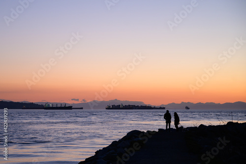 A couple watches the sunset from West Vancouver's Ambleside Park.  West Vancouver British Columbia, Canada.