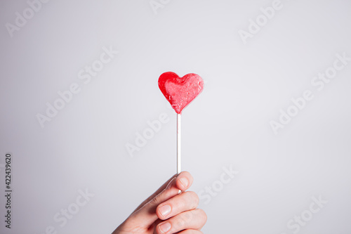 Woman holding bright red heart lollipop isolated on white background.