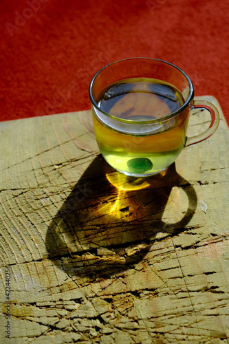 Isolated linden tea cup made of glass and there is green mentholated sweat and candy. Fully linden tea filled glass pot existing on wooden plate and red carpet. photo