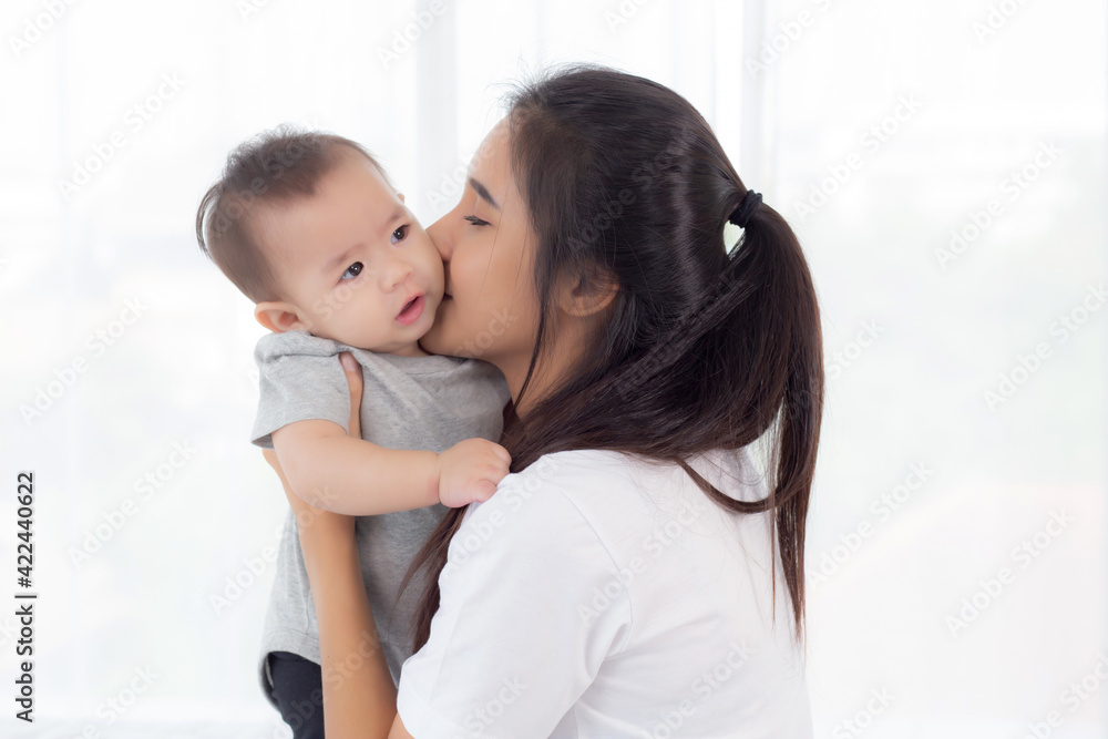 Young asian mother holding little baby girl and kiss together in the bedroom at home, mom carry child and care, woman and kid with carefree, toddler and parent, emotion and expression, family concept. Young asian mother holding little baby girl and kiss together in the bedroom at home, mom carry child and care, woman and kid with carefree, toddler and parent, emotion and expression, family concept.