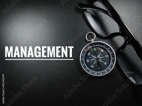 Business concept.Text MANAGEMENT with glasses and compass on black background.