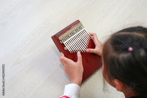 Close-up Asian young hands playing Kalimba (Mbira or thumb piano) lying on wood floor at home. Rear view photo