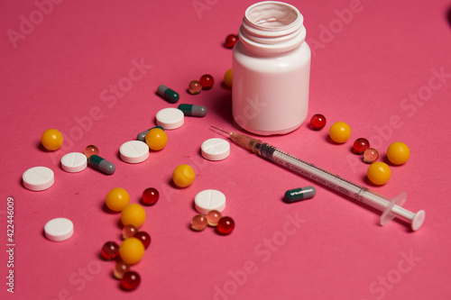 A jar of pills and a syringe with a needle on a pink background side view