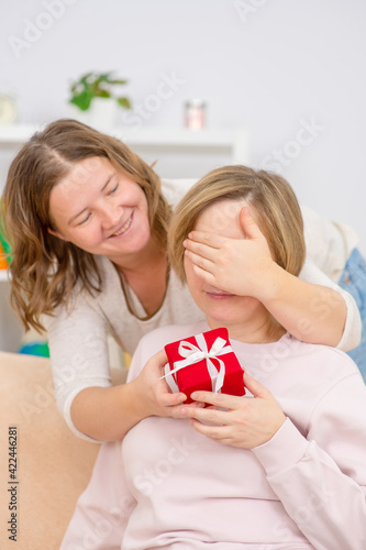 A young woman giving her friend a present and covering her eyes with his hand to surprising. Gay lesbian couple at home. Lesbian couple concept