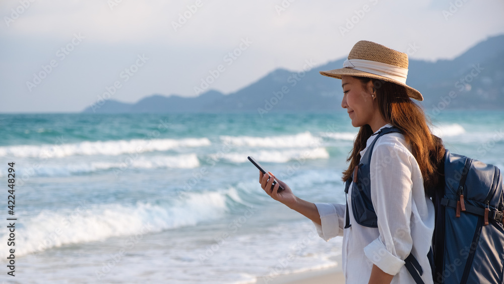 A female traveler holding and using mobile phone while traveling to the sea