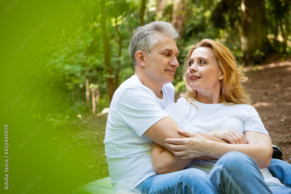 Mature adult happy couple in park hugging while sitting on plaid