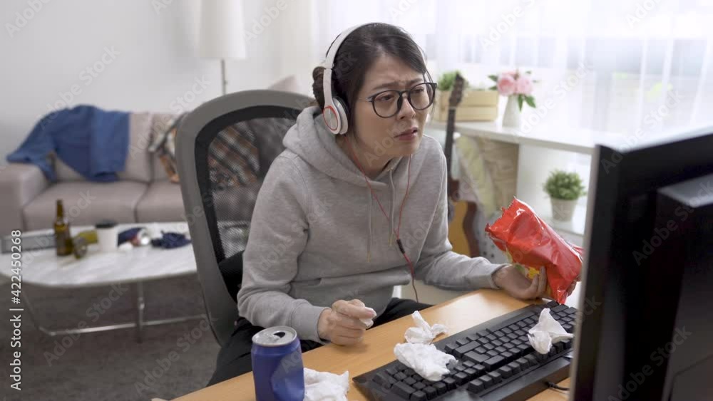 Sad woman watching melodrama movie on computer monitor crying and eating bag of chips. Unhappy asian female wipe tears with tissue while wearing headphones enjoy romantic series online at home. Sad woman watching melodrama movie on computer monitor crying and eating bag of chips. Unhappy asian female wipe tears with tissue while wearing headphones enjoy romantic series online at home.