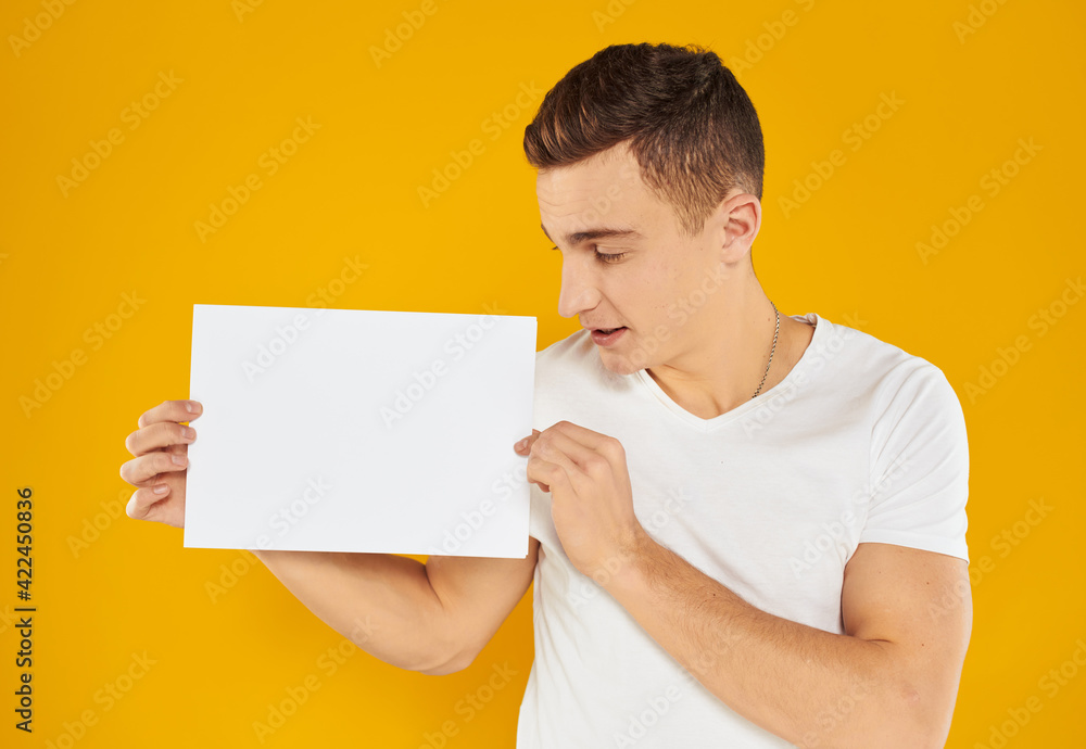 A man on a yellow background with a mockup in his hand a white sheet of paper A man on a yellow background with a mockup in his hand a white sheet of paper