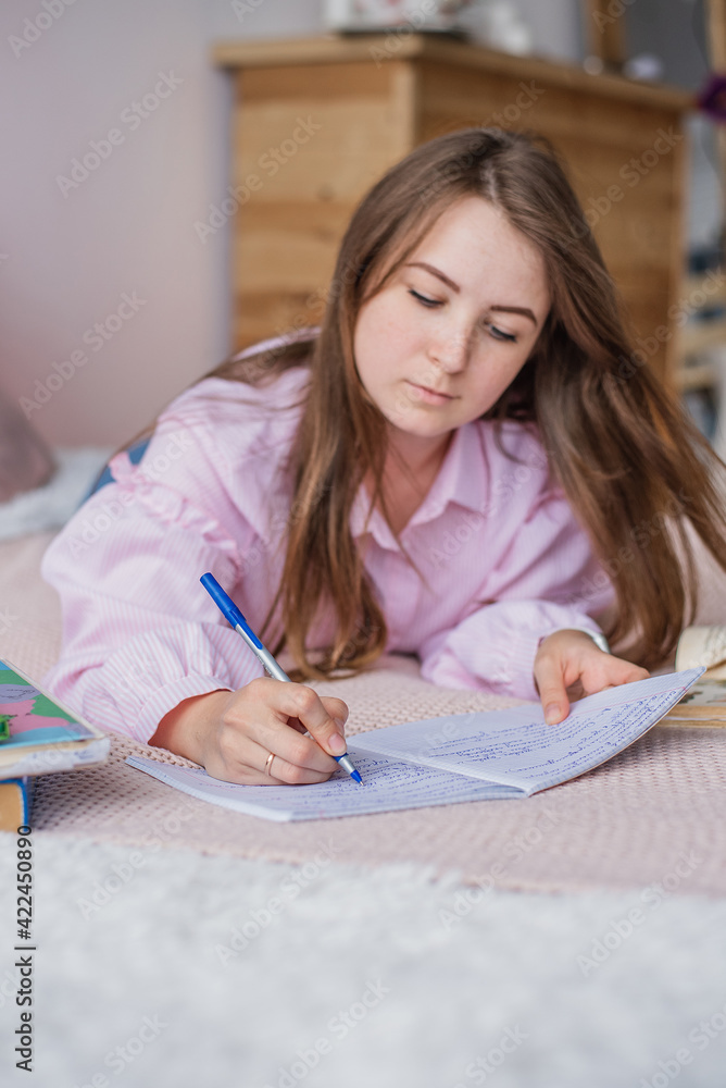 The girl learns in bed, in a bright cozy room, writes in a notebook The girl learns in bed, in a bright cozy room, writes in a notebook
