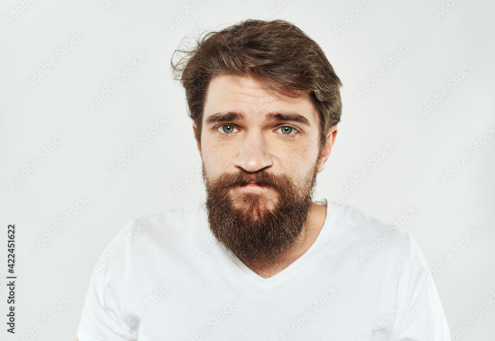 Obraz premium Emotional guy in a white T-shirt on a light background cropped view of a thick beard of a brunette