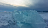Ice shard on a snow-covered lake, close-up. Turquoise transparent shiny hummock against the sunset sky. Lake Baikal. Russia