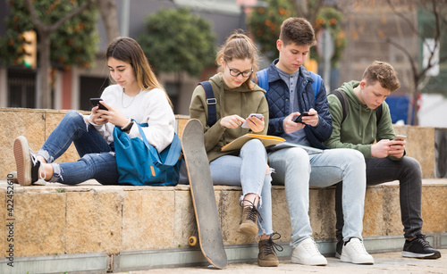 Teenage friends spending time together on streets of city, messaging on their smartphones photo