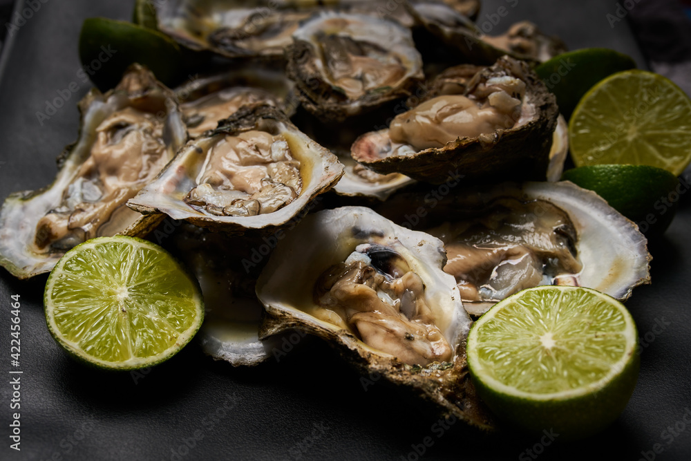 Ostras abiertas, preparadas con limón y sal, puestas sobre un plato cuadrado negro en una tabla de madera
