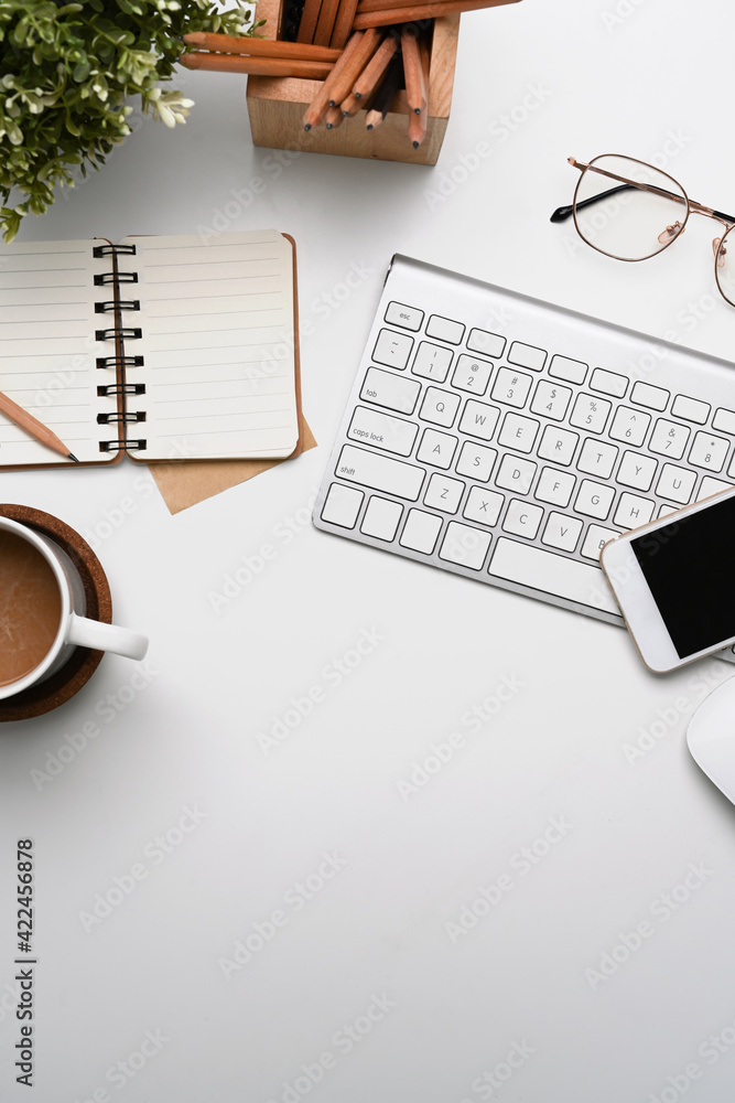 Overhead shot of white office desk with smart phone, notebook, coffee cup, glasses and keyboard. Overhead shot of white office desk with smart phone, notebook, coffee cup, glasses and keyboard.