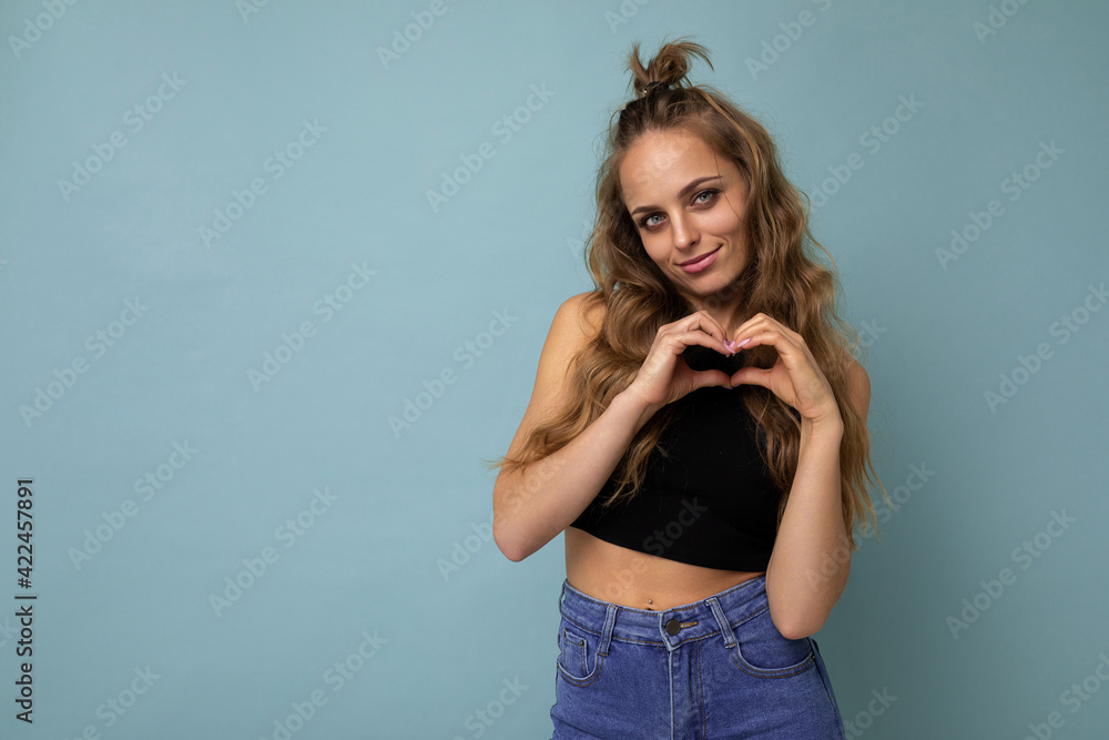 Fototapeta premium Photo of young positive happy smiling beautiful woman with sincere emotions wearing stylish clothes isolated over background with copy space and showing heart gesture