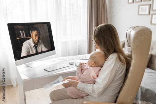 Successful business lady is working from home, having video meeting with colleague. Young mother with a small child in arms discussing work questions about project. Distant work concept