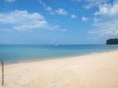 Tropical sandy beach. Empty coast. White sand, clouds on the blue sky, turquoise water of sea. One sailing yachts on the horizon. Calm ocean. Green promontory extending to the deep. Paradise, seascape
