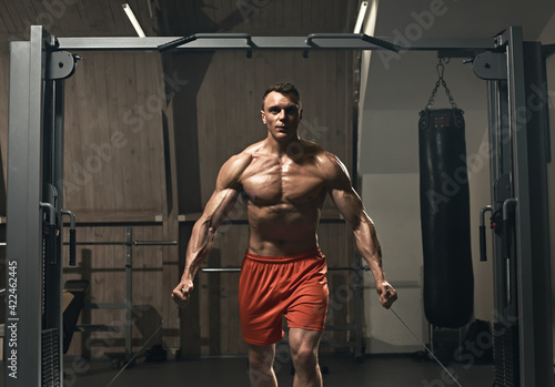 Young handsome sporty bodybuilder exercising with stretching band in gym