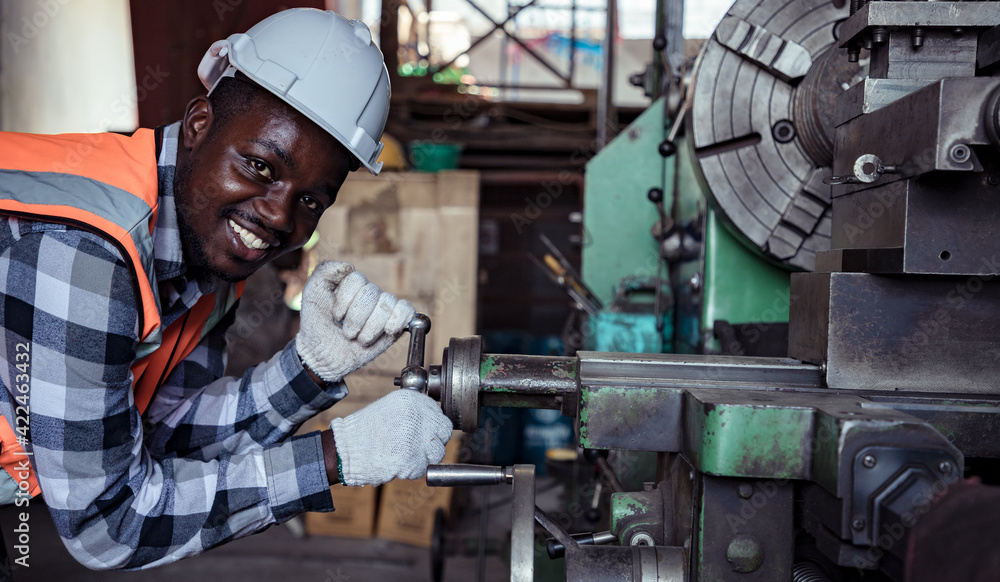 Africa American worker with assistant wearing safety goggles control lathe machine to drill components by wrench. Metal lathe industrial manufacturing factory indoors. Sander concept. Africa American worker with assistant wearing safety goggles control lathe machine to drill components by wrench. Metal lathe industrial manufacturing factory indoors. Sander concept.