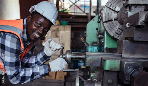 Africa American worker with assistant wearing safety goggles control lathe machine to drill components by wrench. Metal lathe industrial manufacturing factory indoors. Sander concept.