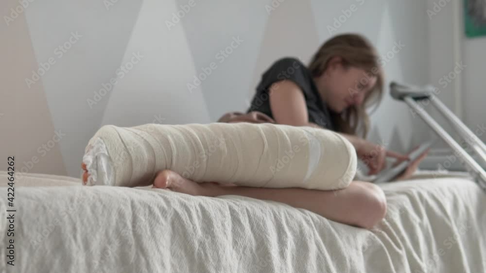 A woman with a large plaster on her leg lies in bed and uses a tablet with the Internet. Focus on plaster, woman blurred in the background A woman with a large plaster on her leg lies in bed and uses a tablet with the Internet. Focus on plaster, woman blurred in the background