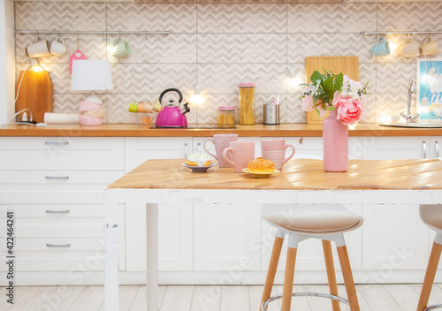 Pink vase with flowers and mugs for tea on the table in a light kitchen