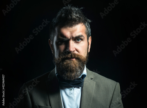 Close up portrait of stylish man with beard and mustache. Guy with serious face in luxury classic suit with bow tie. Barbershop concept
