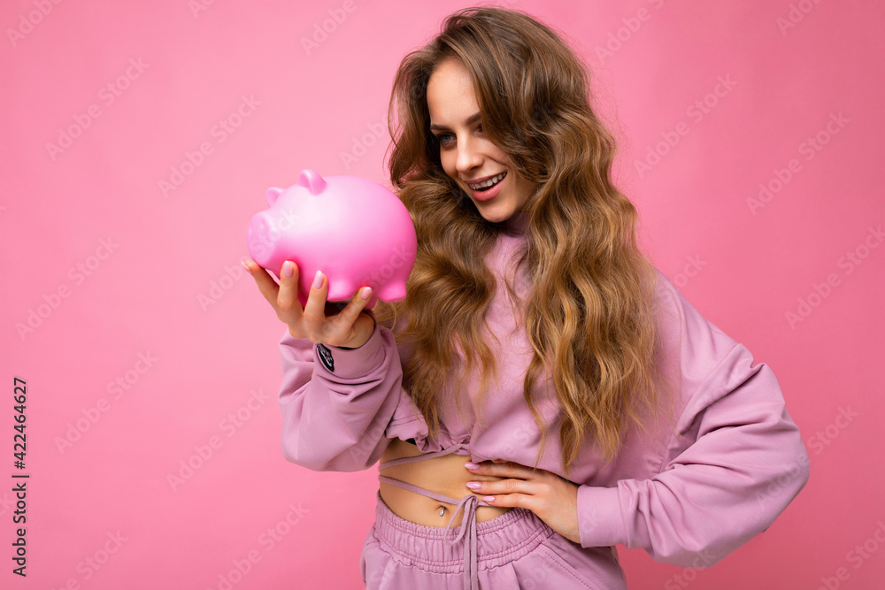 Portrait photo of happy positive smiling young beautiful attractive woman with wavy long blonde hair with sincere emotions wearing stylish pink hoodie isolated over pink background with copy space and Portrait photo of happy positive smiling young beautiful attractive woman with wavy long blonde hair with sincere emotions wearing stylish pink hoodie isolated over pink background with copy space and