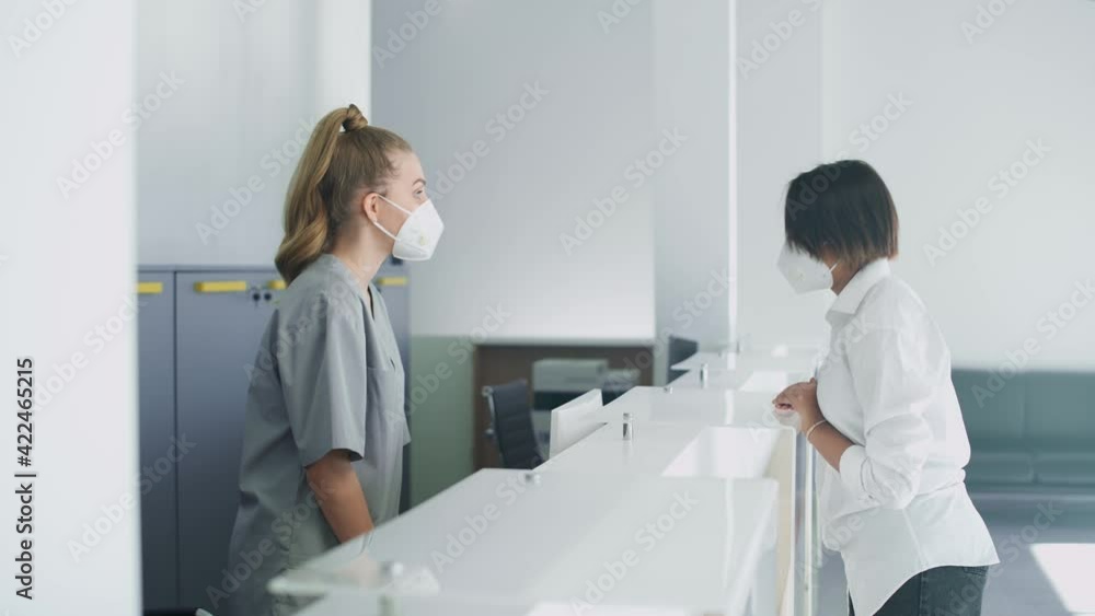 Hospital reception, a nurse registers an young woman patient for a doctor's appointment in a modern medical clinic, people in protective medical masks, coronavirus pandemic. Hospital reception, a nurse registers an young woman patient for a doctor's appointment in a modern medical clinic, people in protective medical masks, coronavirus pandemic.