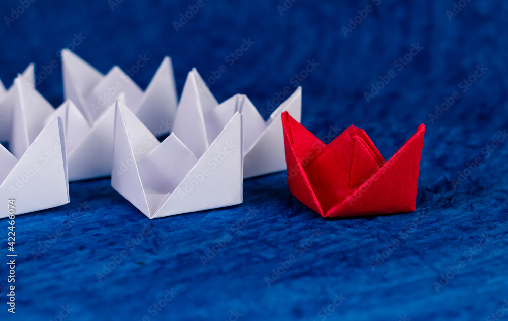 Beautiful close up shot of a red paper boat with white boats on blue paper as ocean.