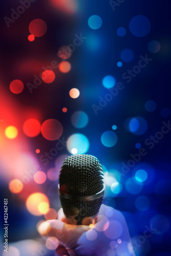 Hand holding a microphone against colourful background.