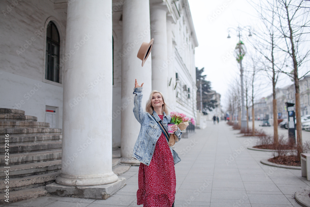Beautiful woman in fashion clothes walking in the street with bouquete of flowers and coffee or tea to go