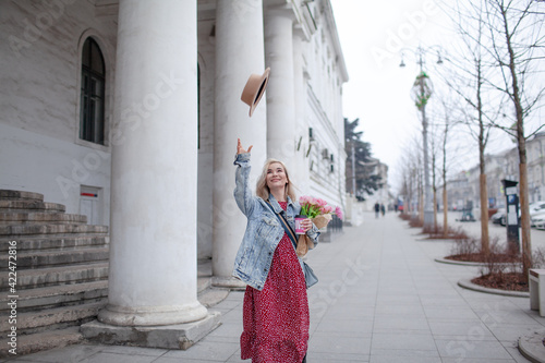 Beautiful woman in fashion clothes walking in the street with bouquete of flowers and coffee or tea to go