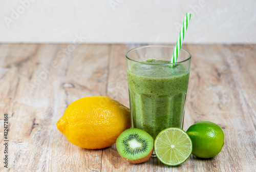 Tall glass with kiwi and spinach smoothie surrounded by fruits on a wooden table