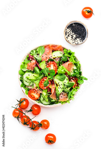 Fresh salad with salted salmon, avocado, cucumber, sesame seeds, olive oil, tomatoes and mixed herbs. White background, top view, copy space