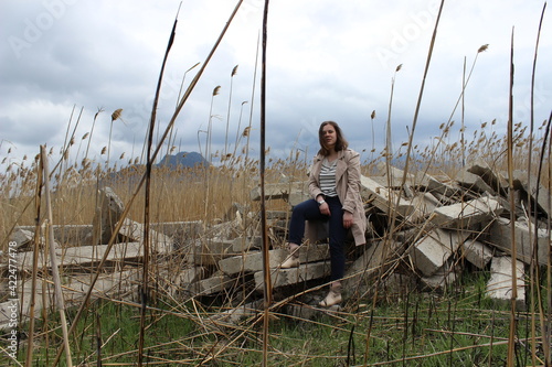 A portrait of an outdoor girl sits in a field on large concrete slabs.