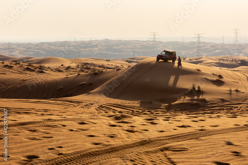 Silhouette of 4x4 car and Arab man in traditional clothes at the top of a sand dune during sunset  Fossil Rock  Sharjah  United Arab Emirates.