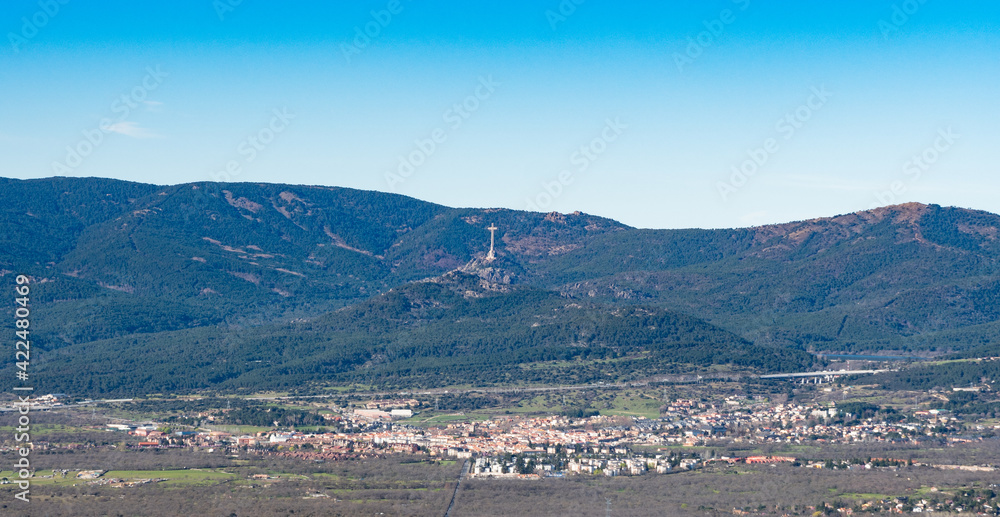 View of the village of Guadarrama with the Cross of the Valley of the Fallen in the background and clear blue sky.