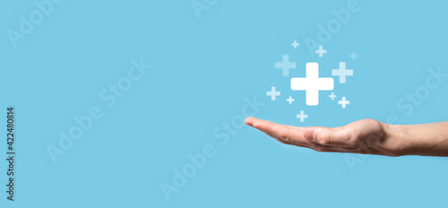 Fototapeta Naklejka Na Ścianę i Meble -  Male hand holding plus icon on blue background. Plus sign virtual means to offer positive thing (like benefits, personal development, social network)Profit,health insurance, growth concepts