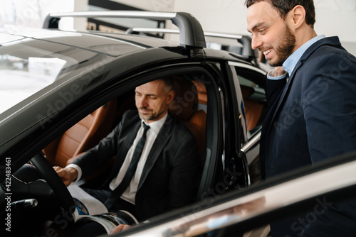 Mid pleased manager showing car to mature customer in showroom