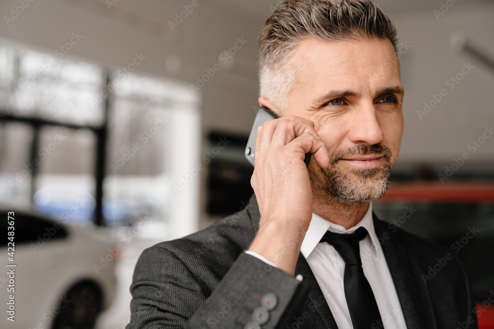 Mature white man talking on cellphone while choosing car in showroom Mature white man talking on cellphone while choosing car in showroom